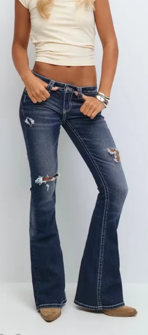 Bootcut jeans med broderade fickor Gina Tricot - Snygga mörkblå bootcut jeans från Gina Tricot med slitna detaljer och broderade bakfickor. Lågmidjade med kontrastsömmar och klassisk femficksdesign. Jeansen har en cool vintagekänsla och är tillverkade i stretchig denim för skön passform.