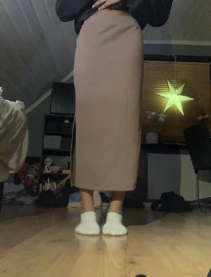 Beige långkjol med slits - Säljer en stilren beige långkjol med rak passform och diskret slits på sidan. Kjolen är enkel och clean i designen, perfekt att styla med sneakers eller boots. Materialet känns mjukt och stretchigt, vilket gör den bekväm att bära hela dagen.