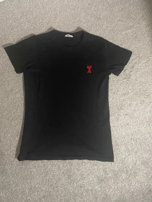 Svart t-shirt från Ami med rött hjärta - Svart t-shirt från Ami Alexandre Mattiussi i storlek S. Klassisk rund hals och korta ärmar. På bröstet finns Ami:s ikoniska broderade röda hjärta med bokstaven A. T-shirten är gjord i mjuk bomull och har en clean, slim passform. Används några gånger och pris kan såklart diskuteras! Den passar både för S och M