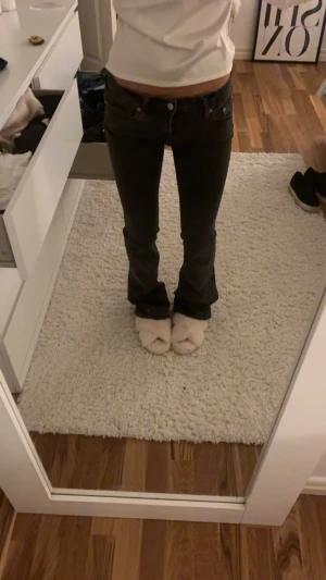 Svarta bootcut jeans  - Säljer ett par svarta jeans med bootcut passform och klassisk femficksdesign. Jeansen har låg midja och är tillverkade i ett slitstarkt jeansmaterial. Snygga detaljer med knappar och dragkedja framtill. Perfekta för dig som gillar en tidlös look.