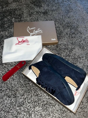 Mörkblå sneakers från Christian Louboutin - Snygga mörkblå sneakers från Christian Louboutin i mjuk mocka med matchande blå snörning och platt sula. Skorna har en stilren och modern design med rund tå och exklusiva detaljer. Perfekta för dig som vill ha något unikt och lyxigt i din skogarderob.