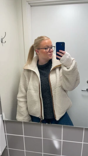 Vit teddyjacka med bruna detaljer - Säljer en fluffig och oversized teddyjacka i vit färg med snygga bruna detaljer längs dragkedjan och ärmarna. Jackan har hög krage, stora fickor och grov dragkedja framtill. Perfekt för dig som gillar chill och trendig stil.