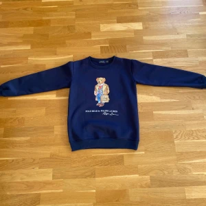 Mörkblå sweatshirt från Polo Ralph Lauren - Säljer en mörkblå sweatshirt från Polo Ralph Lauren med den ikoniska Polo Bear-trycket på bröstet. Tröjan har rund hals, långa ärmar och ribbade muddar vid ärmslut och nederkant. 