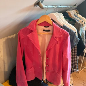 Rosa kavaj Pret á porter - Snygg rosa kavaj från Peak & Pyret med klassisk krage, framfickor och knappar framtill. Jackan har en figurnära passform och är tillverkad i mjukt bomullsmaterial. Perfekt för dig som vill sticka ut med färg och stil.