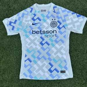 Inter Milan x Nike kortärmad fotbollströja - Snygg Inter Milan fotbollströja från Nike med korta ärmar och Dri-Fit ADV-material som andas. Tröjan har ett geometriskt mönster i vitt, ljusblått och marinblått, samt klubbmärke och sponsortryck på bröstet. Perfekt för dig som vill sticka ut på planen.