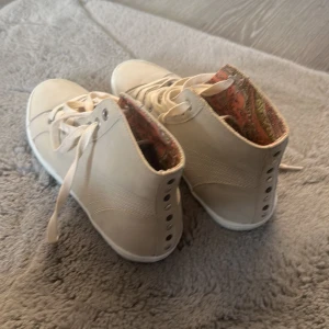 Beiga höga sneakers med mönstrat foder strl 37/38 - Snygga höga sneakers i beige med snörning och rund tå. Skorna har ett färgglatt mönstrat innerfoder som ger en unik touch. Aldrig använda men köpta vinted därav ingen strl o märke men strl skulle jag säga 37-38