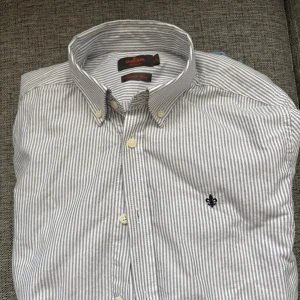 Randig skjorta från Morris - Snygg skjorta från Morris i vitt och grått med smala ränder. Klassisk button-down krage och broderad logga på bröstet.  Storlek M. Helt ny endast provad, digitalt kvitto finns.