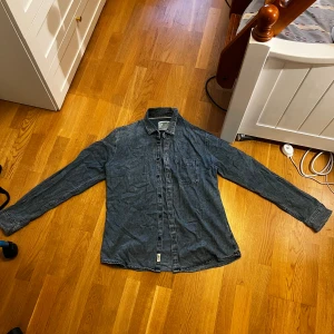 jeansskjorta - Säljer en mörkblå jeansskjorta från Jack & Jones. Skjortan har klassisk krage, knäppning framtill och en bröstficka. Tillverkad i mjukt denimtyg och har långa ärmar. Perfekt för en avslappnad och cool stil.