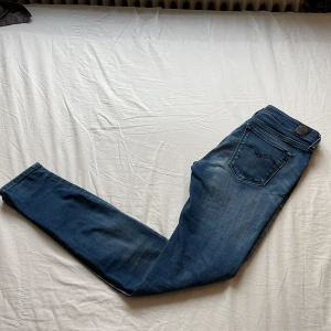 Blå Replay jeans - Snygga blå jeans från Replay med klassisk femficksdesign och diskret slitning. Jeansen har raka ben, normal passform och tydliga Replay-detaljer på bakfickan och läderpatch i midjan. Perfekta för dig som gillar stilrena och bekväma jeans.