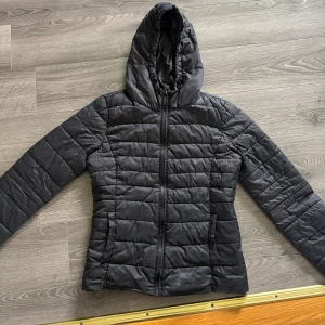 Svart pufferjacka från ONLY med huva - Svart pufferjacka från ONLY i storlek S. Jackan har quiltad design, huva med snörning och hel dragkedja framtill. Perfekt för kyliga dagar och har en stilren look som passar till det mesta. Materialet är syntet och jackan är långärmad. Använd väl💞
