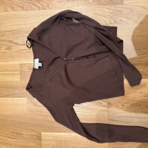 Brun ribbad topp från Pacific Republic - Säljer en brun ribbad topp från Pacific Republic med v-ringning och knappar framtill. Toppen har långa ärmar och är figurnära i modellen. Perfekt att styla med jeans eller kjol för en chill look.