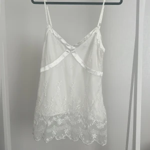 Vitt linne - Ett vitt linne med brodyrdetaljer. Det finns en liten dragkedja på ena sidan för att underlätta när man tar på och av 