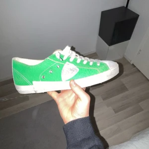 Philippe mod - Snygga gröna sneakers från Philippe Model med vita detaljer och snörning. Skorna har en låg profil, rund tå och vit sula. Materialet är skinn med en texturerad yta och en silverfärgad logotyp på sidan. Perfekta för dig som vill sticka ut med färg på fötterna.