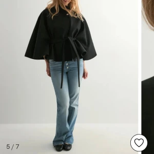Svart ponchokappa Nelly  - Svart kappa med hög krage, vida ärmar och knytbälte i midjan. Stängs med en knapp upptill och har en stilren, loose passform. Perfekt för dig som gillar minimalistisk och trendig look. Aldrig använd från Nelly med prislappar kvar!