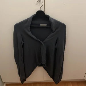 Svart kofta från Hunkydory Essentials - Mysig svart kofta från Hunkydory Essentials med lång ärm och enkel knäppning framtill. Koftan har en avslappnad passform och är stickad i ett mjukt material, perfekt för lager-på-lager under kyliga dagar.