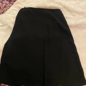 Svart långkjol från DAY - Stilren svart långkjol från DAY med klassisk rak passform. Kjolen har en diskret slits framtill och dragkedja i sidan för enkel påklädning. Perfekt för dig som gillar minimalistisk och tidlös stil.