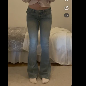 Blå bootcut jeans med låg midja - Säljer ett par ljusblå true religon bootcut jeans med låg midja och klassiska femficksdetaljer. Jeansen har utsvängda ben och snygga sömmar på bakfickorna. Perfekta för dig som gillar retro vibe och vill ha en bekväm passform.💗💗