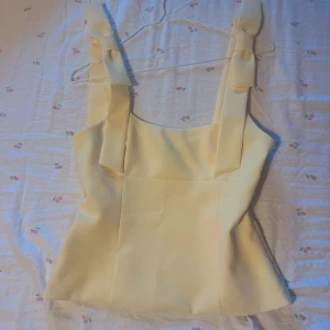 Ljusgul linnetopp med rosetter - Superfin ljusgul linnetopp med breda axelband som knyts i snygga rosetter. Toppen har en rak och figurnära passform med dold dragkedja i sidan. Materialet känns mjukt och har en lätt struktur, helt nu från zara