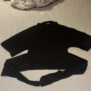 Svart omlottopp från Gina Tricot XS -  från Gina Tricot i mjukt material. Toppen har korta ärmar och långa knytband i midjan som man knyter bakom rygg och använt 1 gång