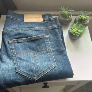 Tiger of Sweden blå jeans herr - Snygga blå jeans från Tiger of Sweden med klassisk femficksdesign och kontrastsömmar. Jeansen har en rak passform och normal midja, tillverkade i slitstarkt denim. Perfekta för dig som gillar stilrena och tidlösa jeans med modern känsla.