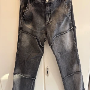 Grå jeans från Fashion Nova - Säljer ett par grå jeans från Fashion Nova med råa sömmar och stora bakfickor. Jeansen har en loose passform och är tillverkade i denim. Snyggt tvättade detaljer och unik design som sticker ut.
