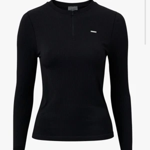 Aim'n Svart ribbad långärmad tröja - Svart långärmad tröja från Aim'n med ribbad struktur och liten metallogo på bröstet. Tröjan har en smal passform, rund hals och half zip-dragkedja framtill. Perfekt för lager-på-lager och snygg till både jeans och tights. Nypris ca 600kr. 