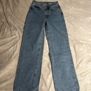 Blå wide jeans från Never Denim - Blå jeans från Never Denim i modellen Regular Wide. Hög midja och raka, vida ben. Klassisk femficksdesign och ljus tvätt.