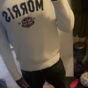 Vit stickad tröja från Morris - Säljer en vit stickad tröja från Morris med mörkblå text och ett snyggt Union Jack-emblem på bröstet.