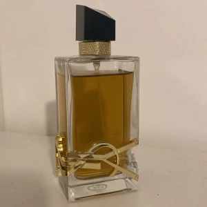 Yves Saint Laurent Libre EdP 90ml - Snygg parfymflaska från Yves Saint Laurent, Libre EdP 90ml. Flaskan är rektangulär i genomskinligt glas med guldig YSL-logga och detaljer, samt svart asymmetrisk kork. Innehållet är bärnstensfärgat. Perfekt för dig som gillar lyxiga och trendiga dofter.