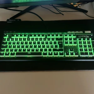 HyperX Alloy Elite 2 RGB Mekaniskt Tangentbord - HyperX Alloy Elite 2 är ett mekaniskt tangentbord med RGB-belysning, dedikerade mediaknappar och volymratt. Tangentbordet är i gott skick med fullt fungerande belysning, men viss damm och smuts syns på ytan. Perfekt för gaming och produktivitet.