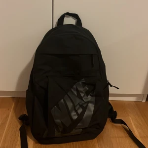 Svart ryggsäck från Nike - Säljer en svart ryggsäck från Nike med stort logotryck på framsidan. Väskan har justerbara axelremmar, bärhandtag upptill och flera fack med dragkedja. Perfekt för skola eller träning och rymmer allt du behöver till vardagen. Säljer då den inte kommer till användning längre 💗