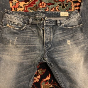 Diesel Safado blå jeans - Snygga blå jeans från Diesel, modell Safado. Jeansen har en klassisk femficksdesign, slitna detaljer och en cool tvättad look. Tillverkade i 100% bomull och har Diesel Industry-märke på bakfickan. Perfekta för dig som gillar en avslappnad och trendig stil.