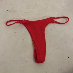 Röd ribbad bikini med knyt - Snygg röd bikini med ribbad struktur. Överdelen är en klassisk triangelmodell med knyt i nacken och ryggen. Underdelen är string och smala band i sidorna. Perfekt för stranden eller poolen. Aldrig använda!