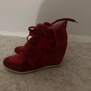 Isabell marant liknande skor - Snygga röda sneakers med kilklack och snörning. Skorna har en mix av mocka och textil, samt kardborreband över vristen. Insidan är fodrad med röd- och vitrandigt tyg. Perfekta för dig som vill ha lite extra höjd men ändå en sportig look.