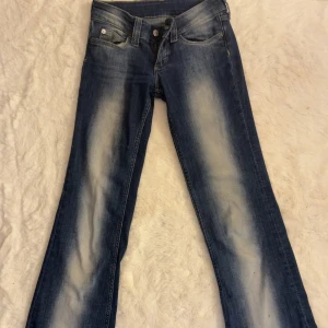Blå jeans med slitningar från Cheap Monday - Säljer ett par blå jeans från Cheap Monday med snygga slitningar och ljusa partier framtill och baktill. Klassisk femficksmodell med bootcut nedtill och låg midjad passform. Jeansen har en cool tvättad look och är tillverkade i jeansmaterial. Storleken är waist:25 Lälng:32