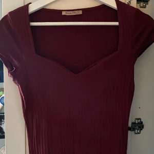 Vinröd ribbad  topp  - Vinröd ribbad topp från Anna Field med snygg v-ringning och korta ärmar. Toppen har en figurnära passform och är perfekt för dig som gillar stilrena och trendiga plagg. Enkel att matcha med accessoarer för en personlig look.