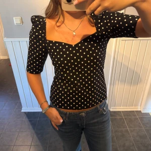Svart prickig topp med puffärm - Säljer en svart topp med vita prickar och snygg sweetheart-urringning. Prislappen är kvar!