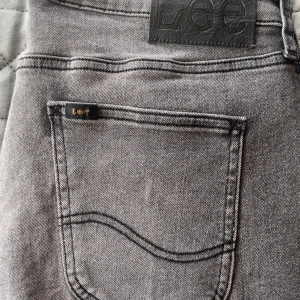 Grå skinny jeans Lee Malone W32 L32 - Snygga grå jeans från Lee, modell Malone, i skinny fit. Klassisk femficksdesign med Lee-logga på bakfickan och svart läderpatch i midjan. Jeansen är tillverkade i stretchig denim för en tajt och bekväm passform. De är endast använda en gång.