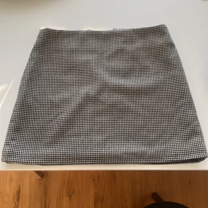 Kjol från HM - Kortkjol från HM i beige och svart pepita mönster. Kjolen har rak passform och är fodrad på insidan samt med dragkedja och knapp bak. 