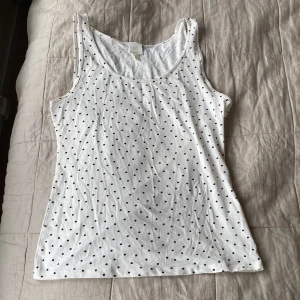 Vit prickig linnetopp från H&M - Säljer en vit linnetopp från H&M med svarta prickar över hela tyget. Toppen är ärmlös med klassisk rund halsringning och tillverkad i mjuk bomull. Perfekt för en enkel och stilren look.