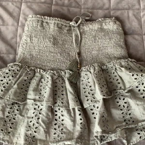 Beige volangkjol från Zara XS - Supersöt beige kortkjol från Zara i storlek XS. Kjolen har smockad midja med knytband och tofsar, samt två lager volanger med broderade hålmönster. Perfekt för en chill sommardag eller när du vill känna dig extra söt. säljer bara om du följer mig💞