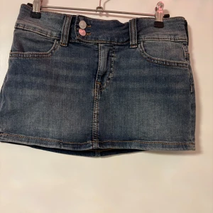 Blå jeanskjol med fickor - Snygg blå jeanskjol från Hm med klassisk femficksdesign, bälteshällor och dubbla silverknappar fram. Kjolen är kort och har en rak passform, perfekt till sneakers eller boots. Tidlös denim-look som alltid funkar.