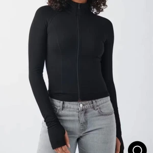 Svart slim jacka med dragkedja - Snygg svart jacka i slim fit med hel dragkedja framtill och långa ärmar. Jackan har en minimalistisk look och är tillverkad i ett stretchigt material som sitter tajt mot kroppen. Perfekt för dig som gillar en clean och sportig stil.