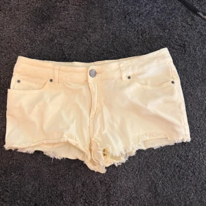 Gula  jeansshorts med fransig kant - Snygga gula  jeansshorts med fransig kant nertill. De har knapp och dragkedja framtill samt bälteshällor. Perfekta för varma dagar när du vill ha en avslappnad och trendig look.
