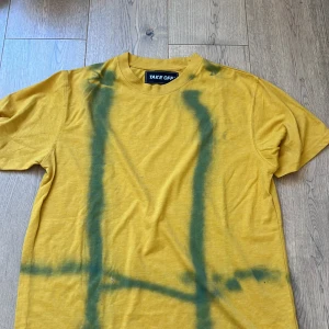 Gul t-shirt med grönt mönster Take Off - Cool gul t-shirt från Take Off med unikt grönt spraymönster framtill. Klassisk passform med rund hals och korta ärmar. Tillverkad i en mjuk mix av polyester och bomull som känns skön mot huden. Perfekt för dig som vill sticka ut med en färgstark look.