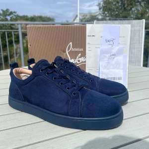 Mörkblå sneakers från Christian Louboutin - Snygga mörkblå sneakers i mocka från Christian Louboutin med klassisk röd sula och diskret logga på hälen. Skorna har rund tå, platt sula och snörning. Insidan är i beige skinn och sulan har den ikoniska Louboutin-signaturen.