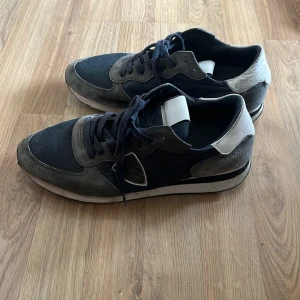 Philippe Model sneakers i blå och grå mocka - Snygga sneakers från Philippe Model i en mix av blå textil och grå mocka med vita detaljer på häl och plös. Skorna har klassisk snörning, rund tå och platt sula. Perfekta för dig som gillar en sportig och stilren look. (Använt 2 gånger inget mer pris kan diskuteras 