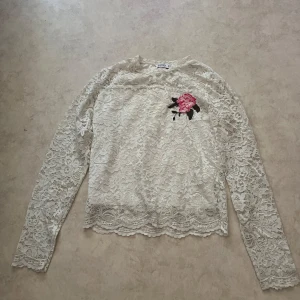 Vit spetsblus med broderad ros från WOW - Superfin vit spetsblus från WOW i storlek M-L. Blusen har långa ärmar, helspets och en broderad rosa ros med gröna blad på bröstet. Perfekt för dig som gillar romantiska detaljer och vill sticka ut lite extra. Den är nog M-L i barnstolek men xs i vanlig storlek.