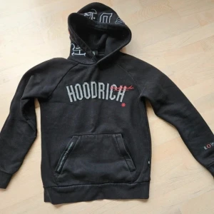 Hoodrich hoodie  - Svart hoodie från HOODRICH med stor broderad logga på bröstet och tryck på ärmen. Huva med broderade detaljer och känguruficka framtill. Mjuk bomullsmix, långärmad och loose fit. Snygga kontrastdetaljer i rött och vitt.