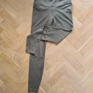 Nike Dri-Fit gröna leggings - Snygga gröna leggings från Nike med Dri-Fit-teknologi. De har hög midja och en tight passform som sitter skönt vid träning. Diskret Nike-logga på benet och stretchigt material som andas.